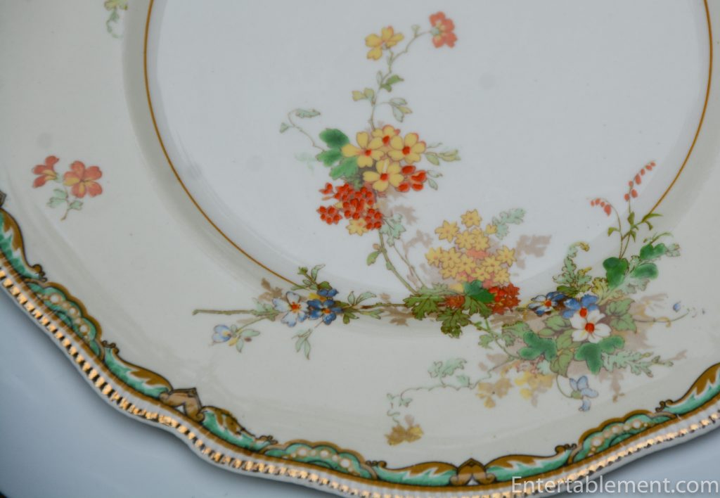 Close-up of Ningpo Pareek pattern showing yellow, red, and blue floral clusters along the rim with gold trim and scalloped turquoise border detail.
