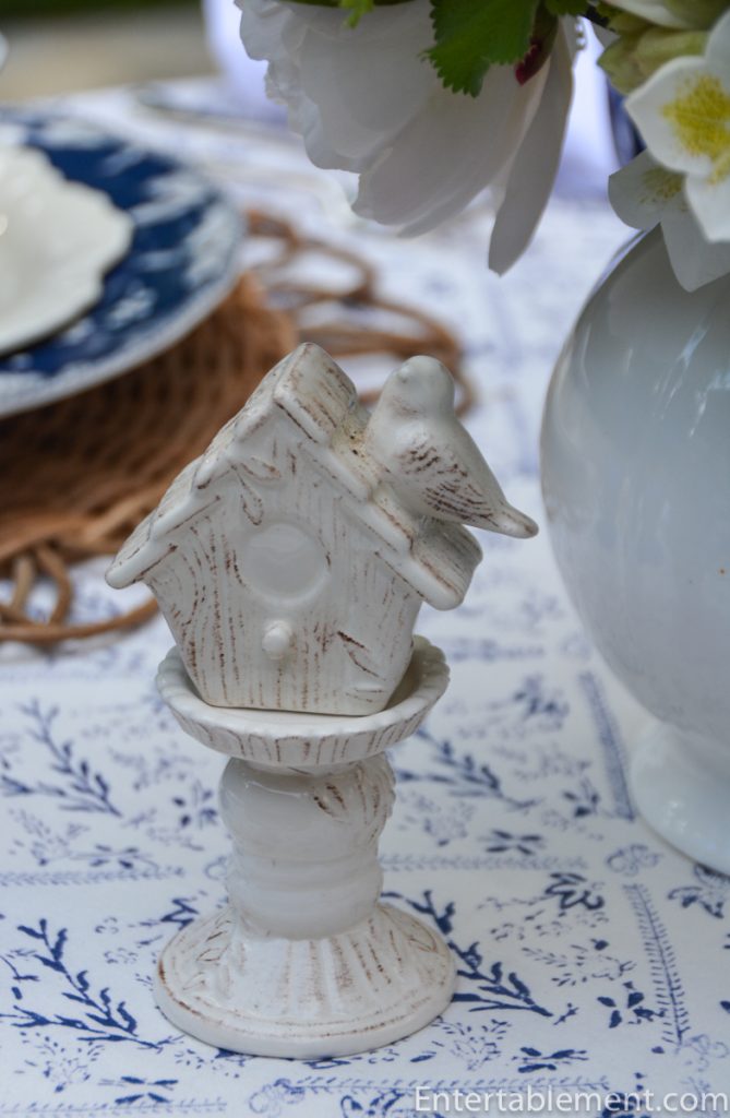 White ceramic birdhouse salt and pepper shaker with bird figurine on blue and white botanical tablecloth.