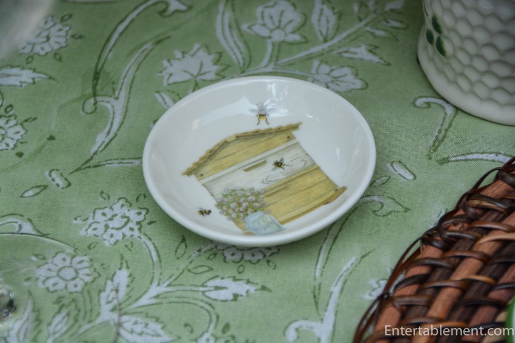 Small porcelain bee and beehive dish beside fresh Limelight hydrangeas on a pale green floral tablecloth.