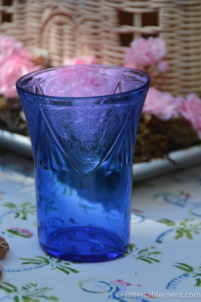 Etched cobalt blue Hazel Atlas Royal Lace tumbler on a printed tablecloth featuring whimsical bicycle illustrations.