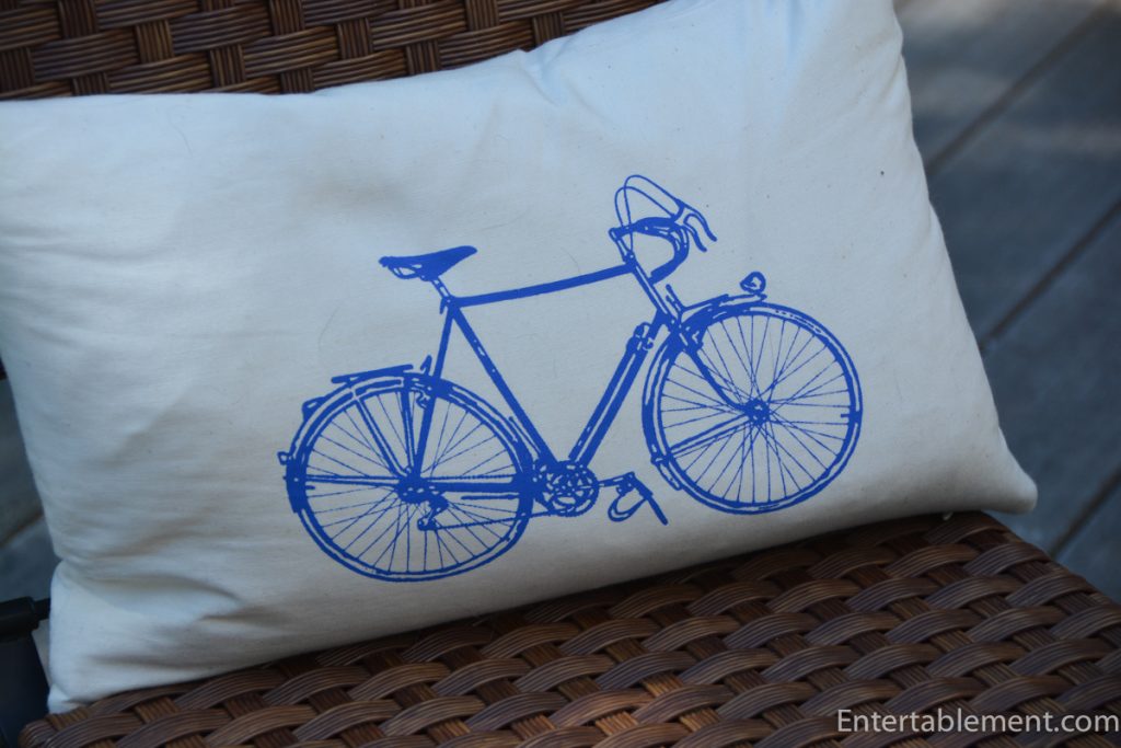 Decorative cream-colored pillow with a blue vintage bicycle print on a woven chair