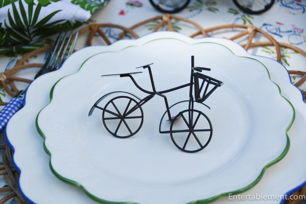 Close-up of scalloped white plate with green trim, topped with a miniature black bicycle sculpture.