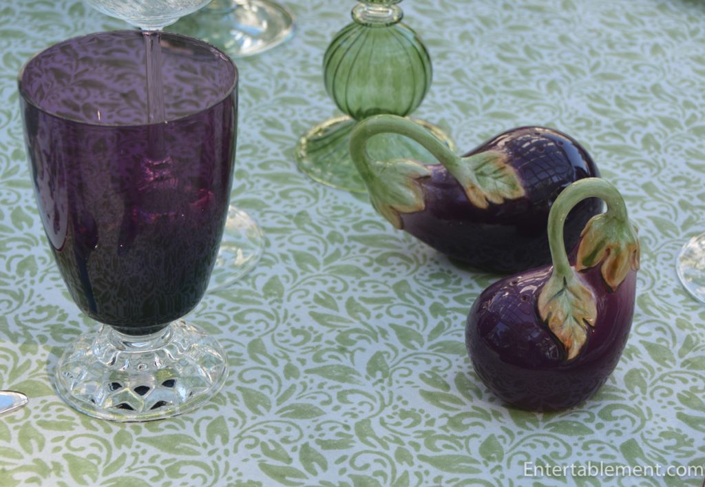 Chelsea porcelain vegetable-patterned dinner plate set with antique-style silver flatware and small ceramic pea-pod and aubergine ornaments.