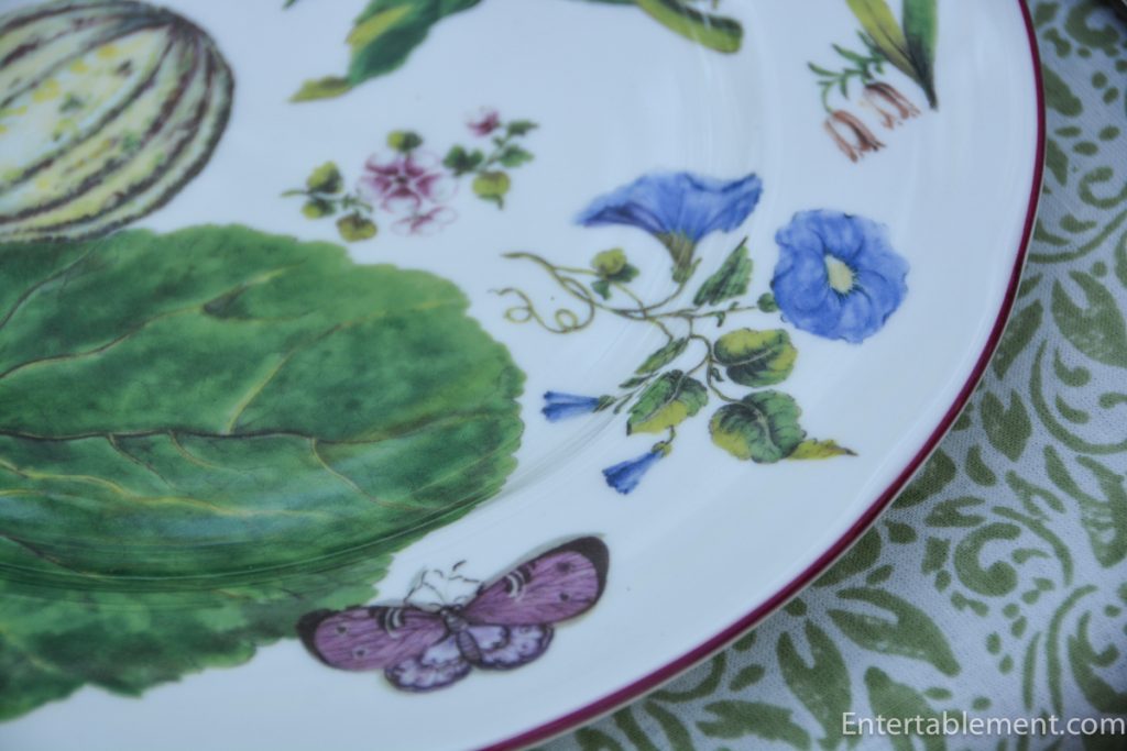 Close-up of Chelsea porcelain plate showing a green leaf, blue flower and purple butterfly against a pale green scrolling tablecloth.