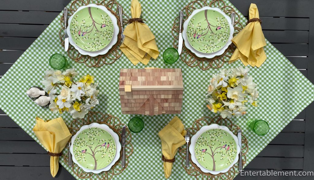Spring bird-themed table setting with green gingham tablecloth, yellow napkins, daffodils, and a birdhouse centerpiece