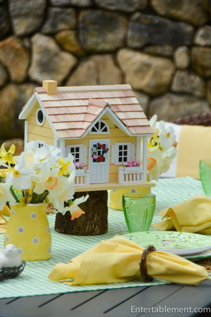 Spring table with raised birdhouse centerpiece, daffodils, and coordinated green and yellow place settings