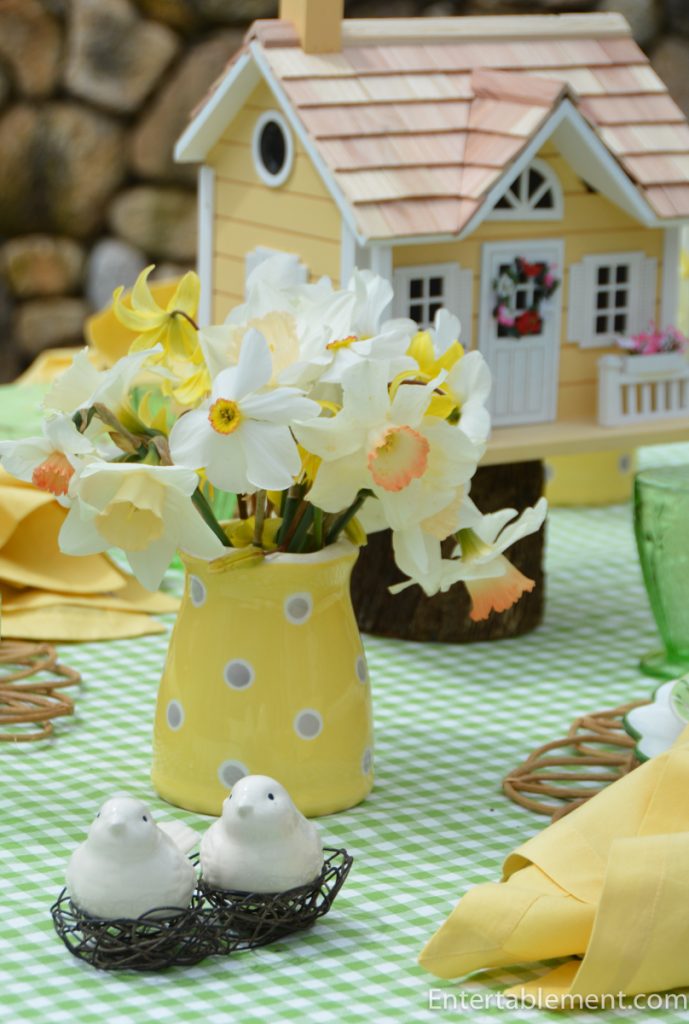 Yellow polka dot pitcher filled with daffodils on a spring table with bird décor and green gingham cloth 