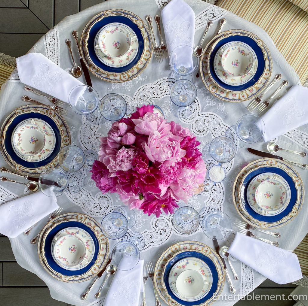 Overhead view of table with French blue and gold Spode plates, Limoges charger, and peony centerpiece with Venetian glassware.