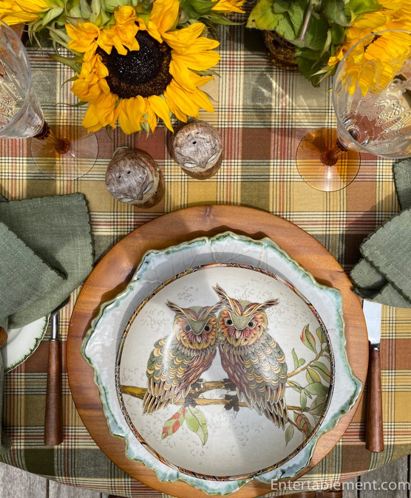 Close-up of pasta bowl with two stylized owls, surrounded by amber glassware and bright yellow sunflowers.