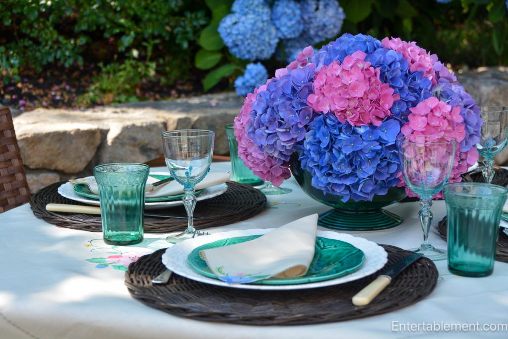 Bold centrepiece of pink and blue hydrangeas surrounded by Turquoise Jeanette Doric and Pansy Depression glass and vintage majolica leaf plates.