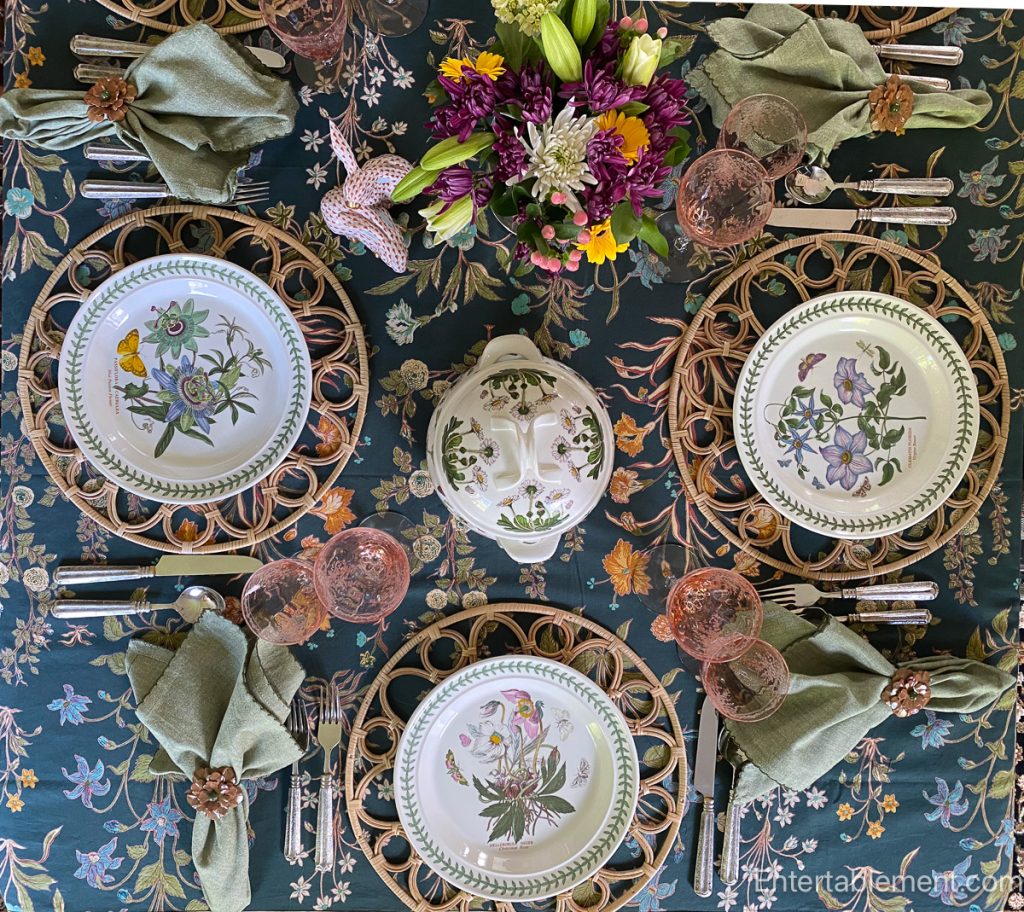 Overhead shot of three Botanic Garden plates with pink glassware, green napkins, and a floral tablecloth.
