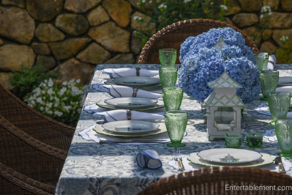 Tablescape styled with Mrs. Alice blue pagoda plates, paired with scalloped white placemats by Rebecca Udall and vintage pink Cherry Blossom glassware by Jeanette. The centerpiece features lush blue hydrangeas in a white vessel, flanked by classic blue-and-white chinoiserie lanterns from The Enchanted Home. An elegant blend of whimsical and formal, set outdoors for a summer luncheon.
