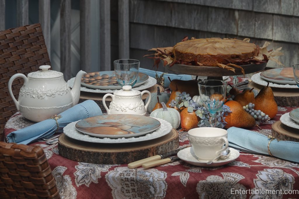 Pear-Maple Upside-Down Cake on a wooden pedestal surrounded by pears, autumn leaves, and a Wedgwood tea service on a russet paisley cloth.