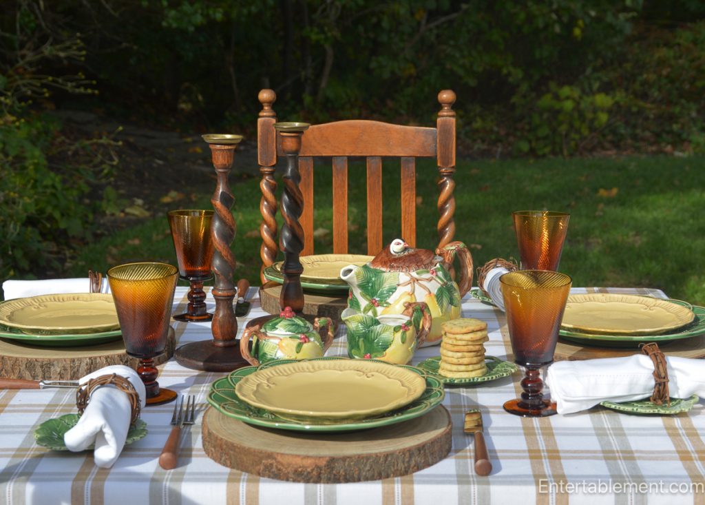 Rustic outdoor fall tea table with Bordallo Pinheiro partridge-and-pear tea set, amber stemware, wooden candlesticks, and leaf-themed plates.