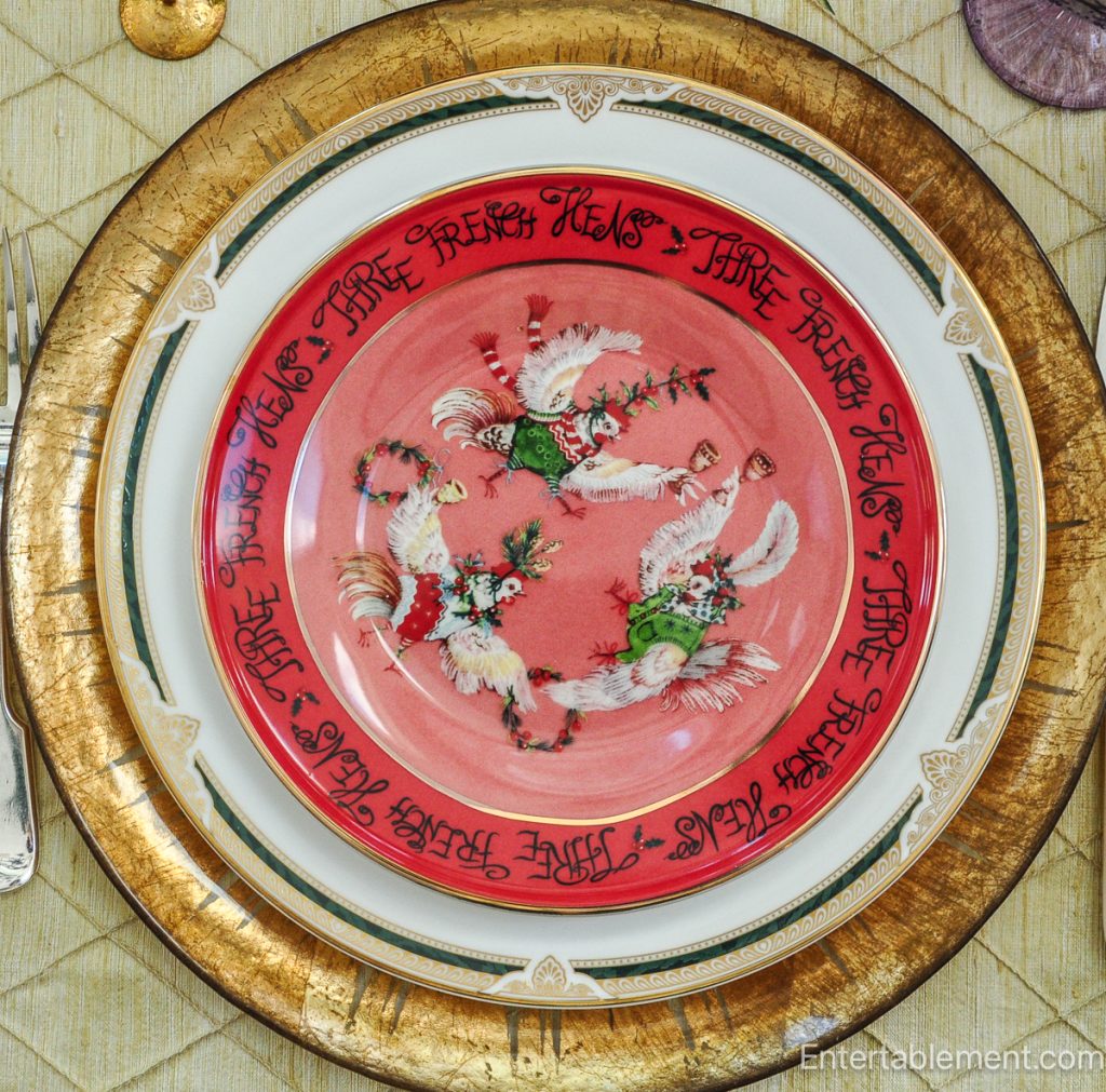 Anthropologie ‘Three French Hens’ plate in red with stylized hens and holiday greenery, shown on gold charger.