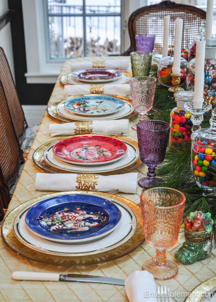 Side view of the full Christmas tablescape, showing gold chargers, white linens, pastel goblets, and the candy-laden centrepiece running the length of the table.