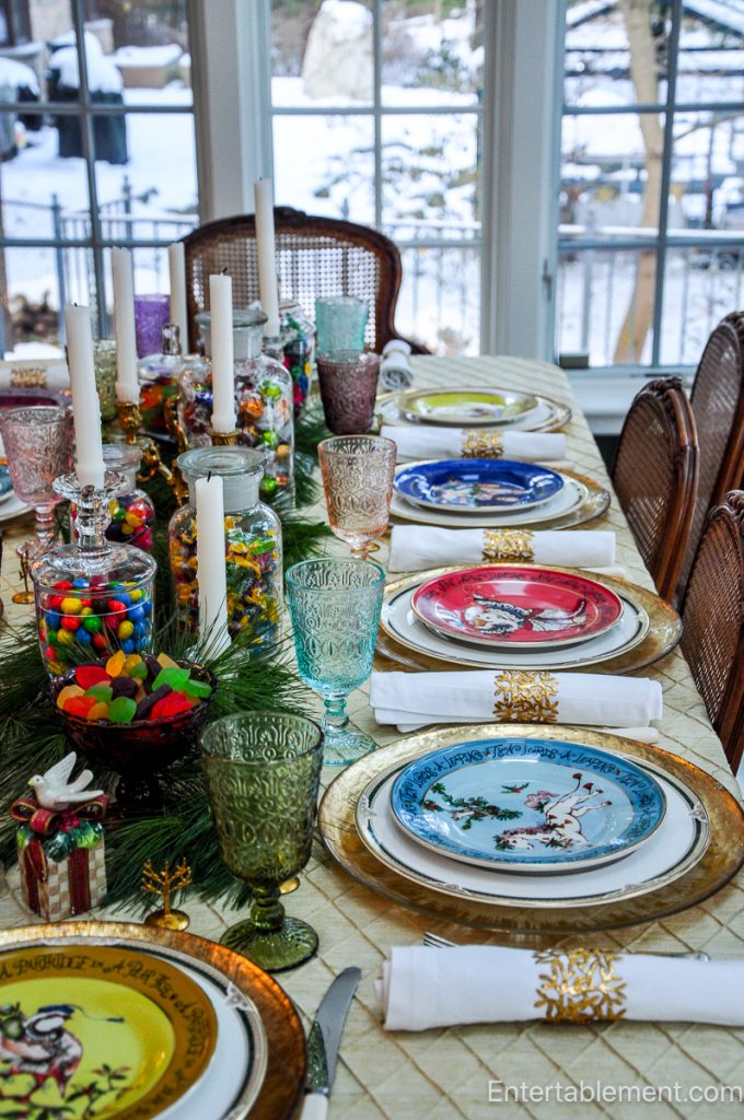 Side view of the full Christmas tablescape, showing gold chargers, white linens, pastel goblets, and the candy-laden centrepiece running the length of the table.