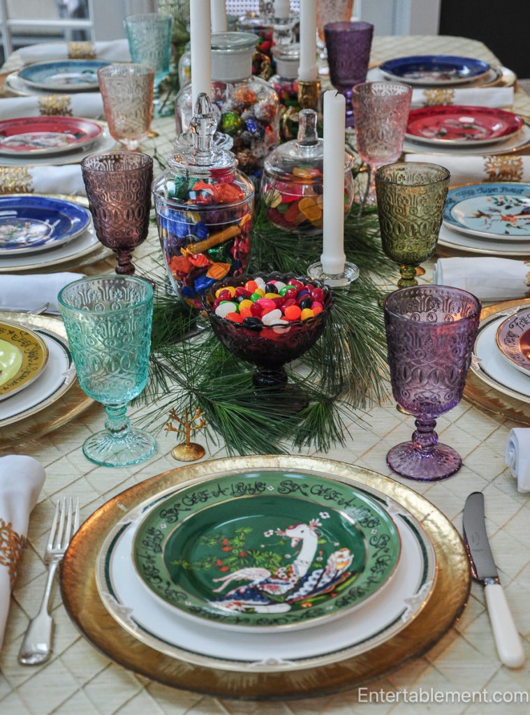 Cluster of candlesticks, pine branches, and candy jars adding height and texture to the Christmas table.