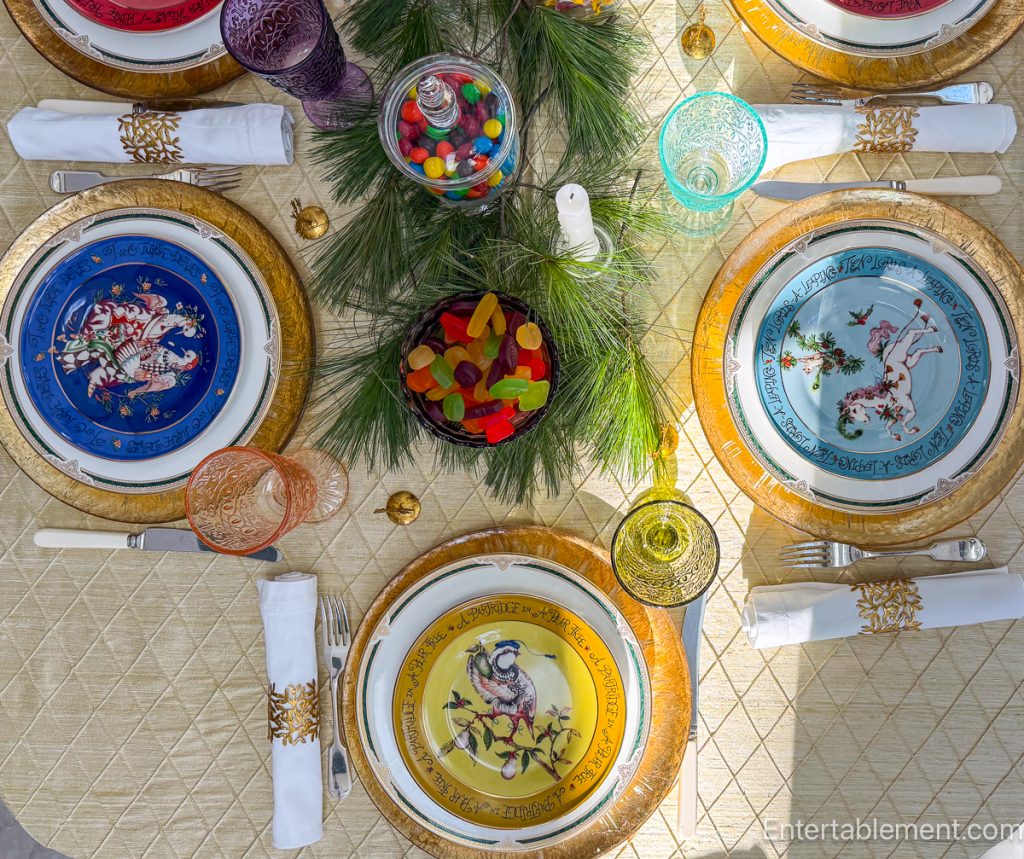Pressed-glass goblets in assorted jewel tones surrounding jars of Christmas sweets and pine greenery.