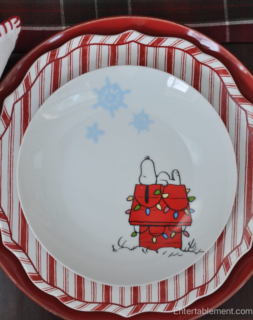 Peanuts Christmas plate showing Snoopy lying on top of his red doghouse decorated with colourful Christmas lights and blue snowflakes overhead.