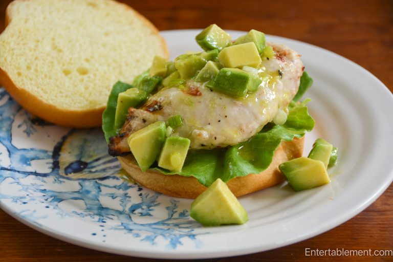 Grilled chicken burger on a toasted brioche bun with butter lettuce and avocado, ginger, and wasabi salsa, served on a blue-and-white plate.
