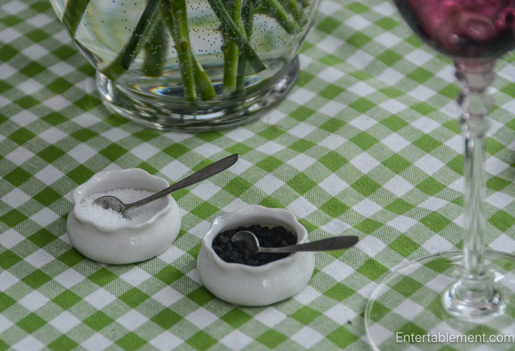 Small white ceramic salt and pepper dishes on a green gingham tablecloth.