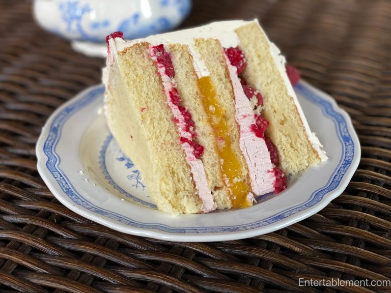 Slice of lemon raspberry layer cake with lemon curd, raspberries, and pale frosting on a blue-and-white plate