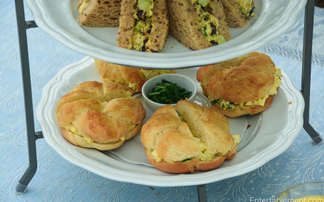 Traditional afternoon tea sandwiches including curried chicken and egg salad on tiered serving tray