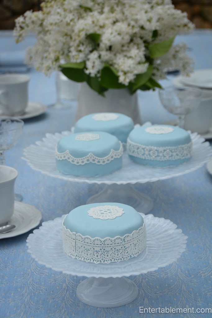 Pale blue decorated cakes with edible lace details arranged on milk glass stands
