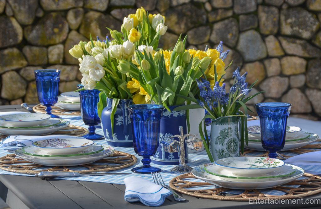 Wide view of an outdoor spring table set with blue and white tableware, spring flowers, and melting snow in the background