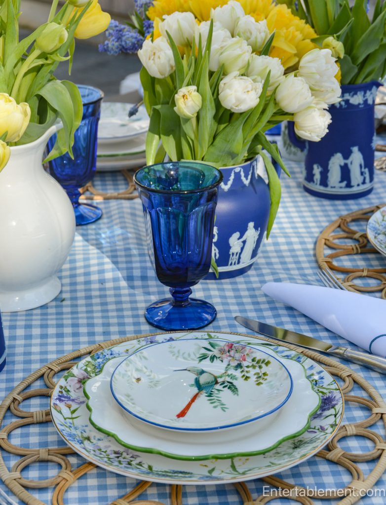 Detail of cobalt blue goblet and spring flowers on a blue gingham outdoor table