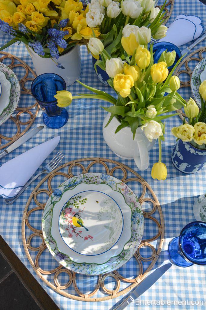Layered place setting with floral plates, woven placemat, and blue goblet on a blue gingham tablecloth