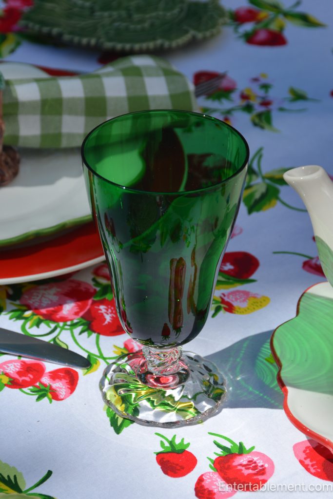 Emerald green goblet casting colorful reflections across an April Cornell strawberry tablecloth.