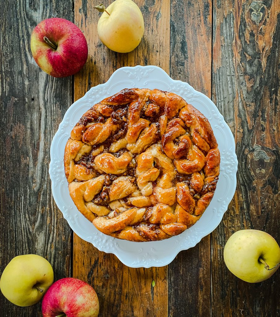 Overhead view of Apple Pecan Sticky Bread featuring glossy twists of apple butter and toasted pecan filling on a white platter.