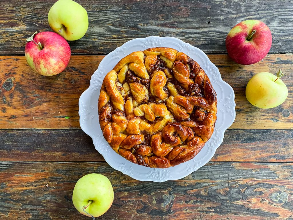 Golden Apple Pecan Sticky Bread glazed with apple jelly and presented on a white serving platter with fresh autumn apples.