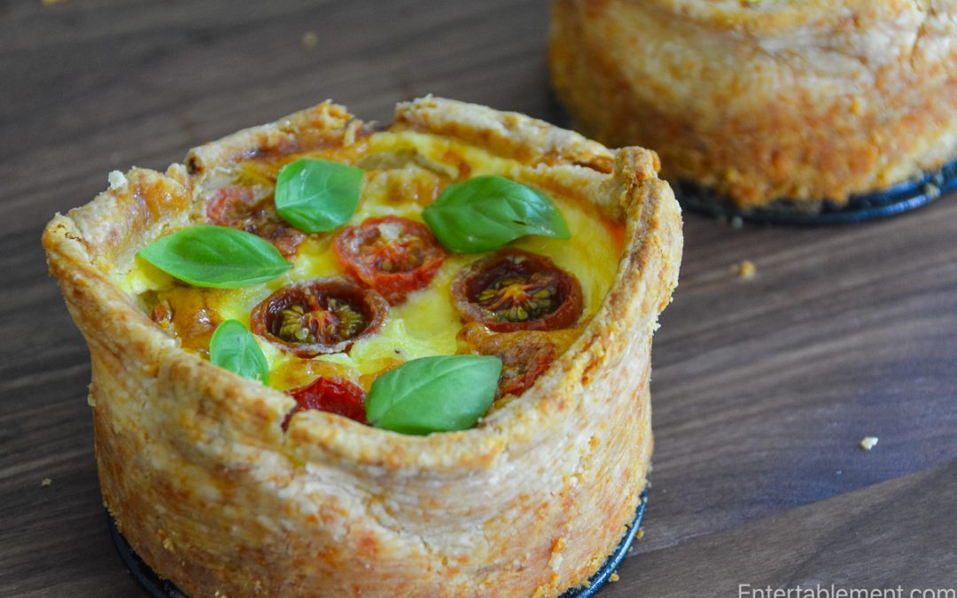 Close-up of a tomato, corn and basil tart showing its tall, flaky Cheddar pastry shell and golden savoury custard.