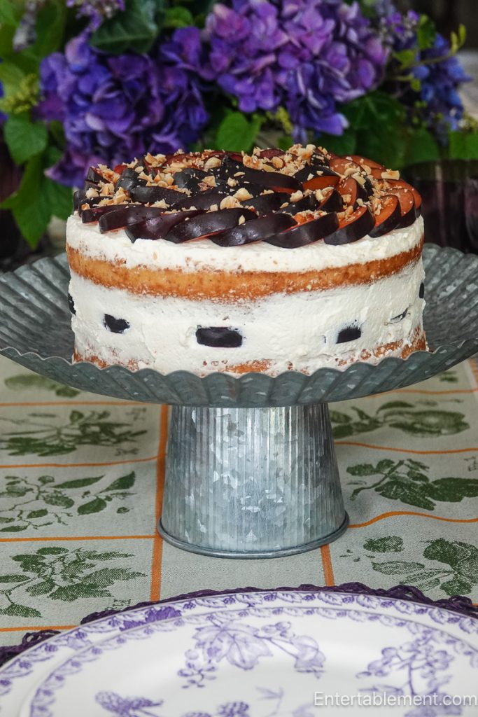 Plum Hazelnut Cream Cake decorated with overlapping fresh plum slices and toasted hazelnuts for a late summer dessert. 