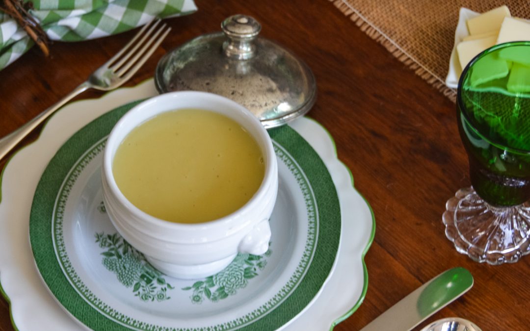 Creamy potato leek soup in a white soup bowl on a green transferware place setting with emerald glassware.