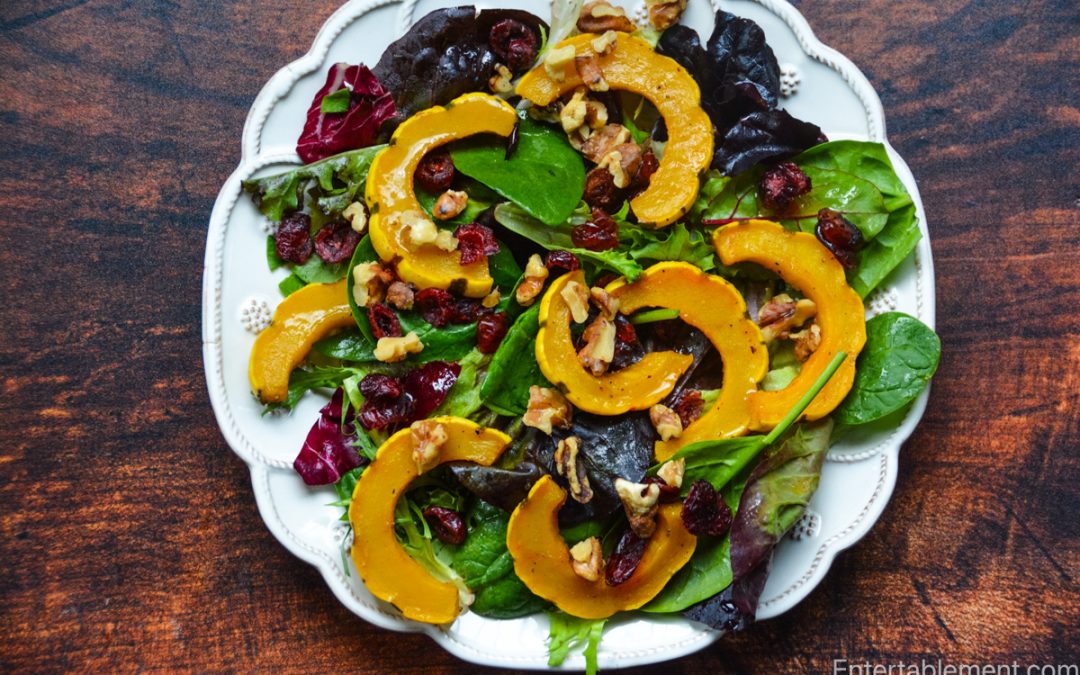 Roasted delicata squash salad with mixed greens, toasted walnuts, dried cranberries and maple vinaigrette served on a white platter.