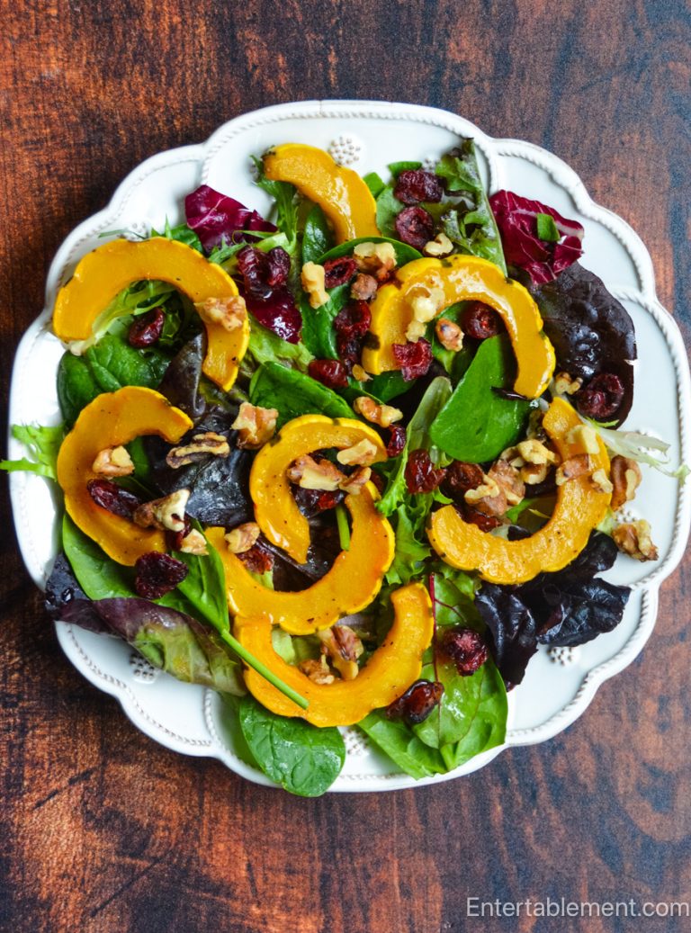 Roasted delicata squash salad with mixed greens, toasted walnuts, dried cranberries and maple vinaigrette served on a white platter.
