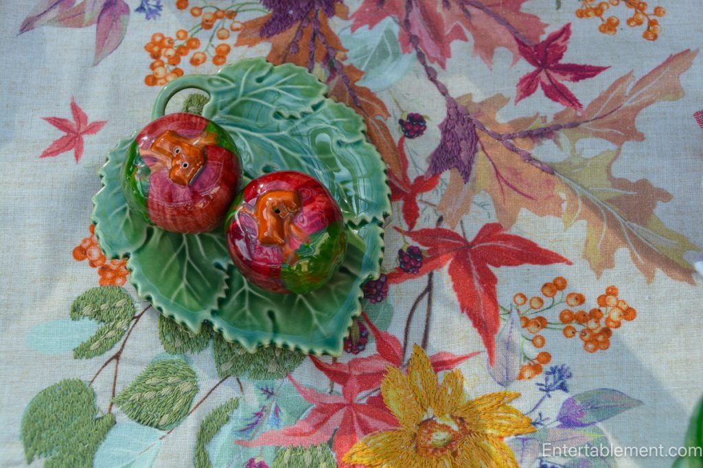 Burgundy and green autumn place setting beside an embroidered runner scattered with colourful leaves and berries.