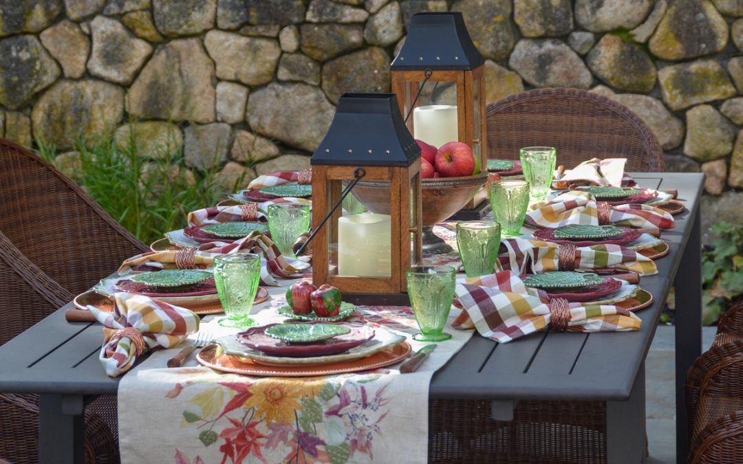 Autumn garden table with an embroidered leaf runner, burgundy plates, green glassware, apples and wooden lanterns.