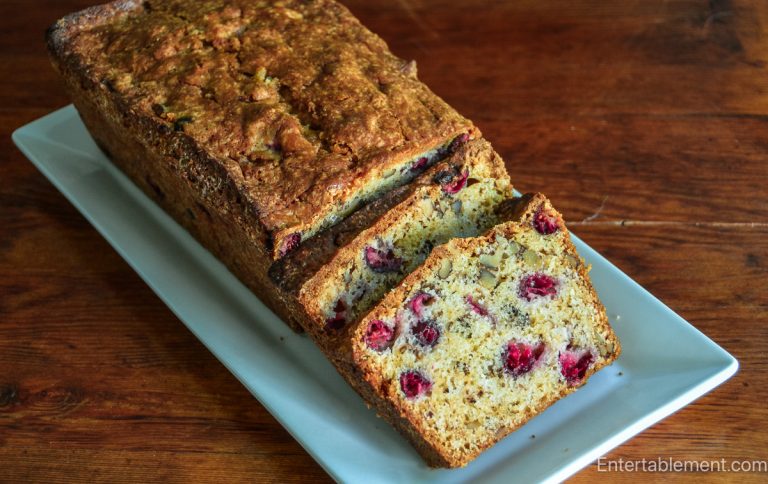 Golden Cranberry Orange Walnut Loaf with cut slices revealing cranberries and walnuts on a wooden table.