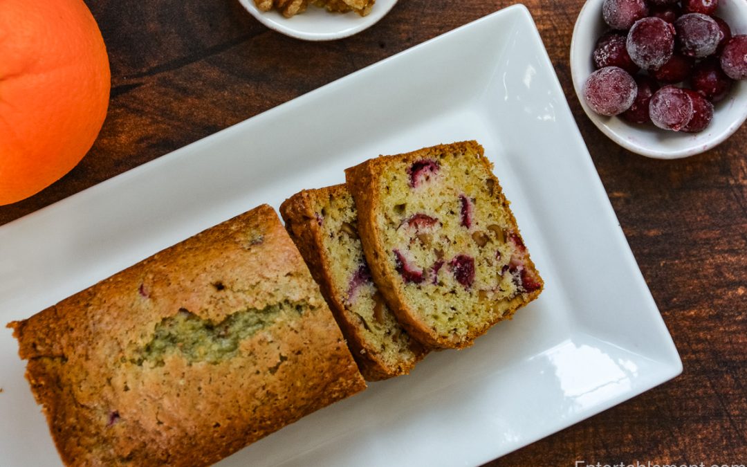 Cranberry Orange Walnut Loaf with sliced loaf, fresh cranberries, walnuts and orange on a white platter.