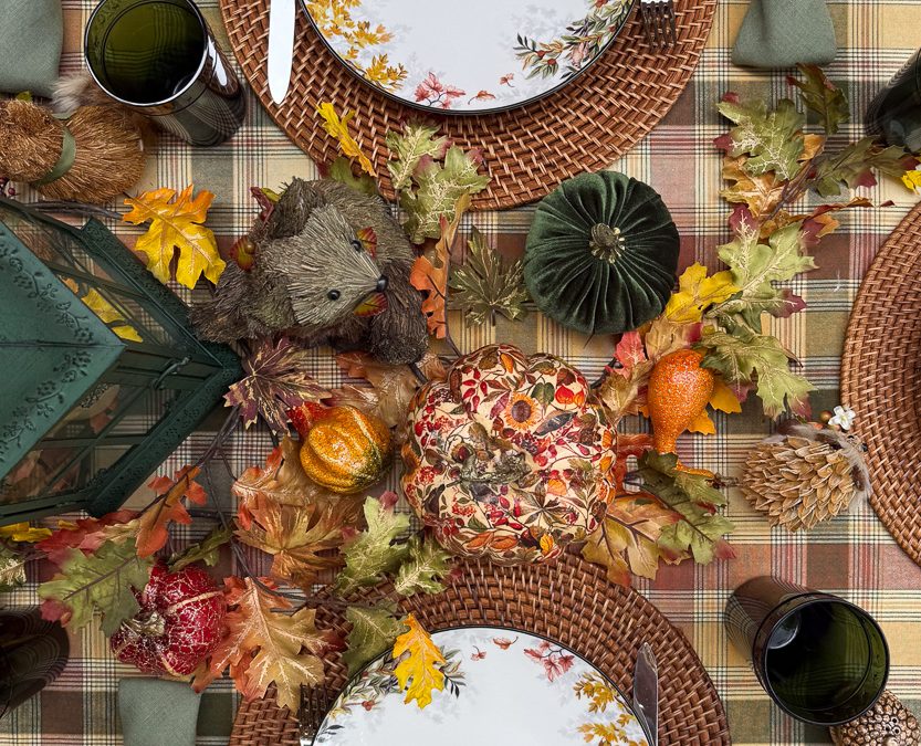 Overhead autumn table detail with a hedgehog, patterned fabric pumpkin, green velvet pumpkin and woodland china.