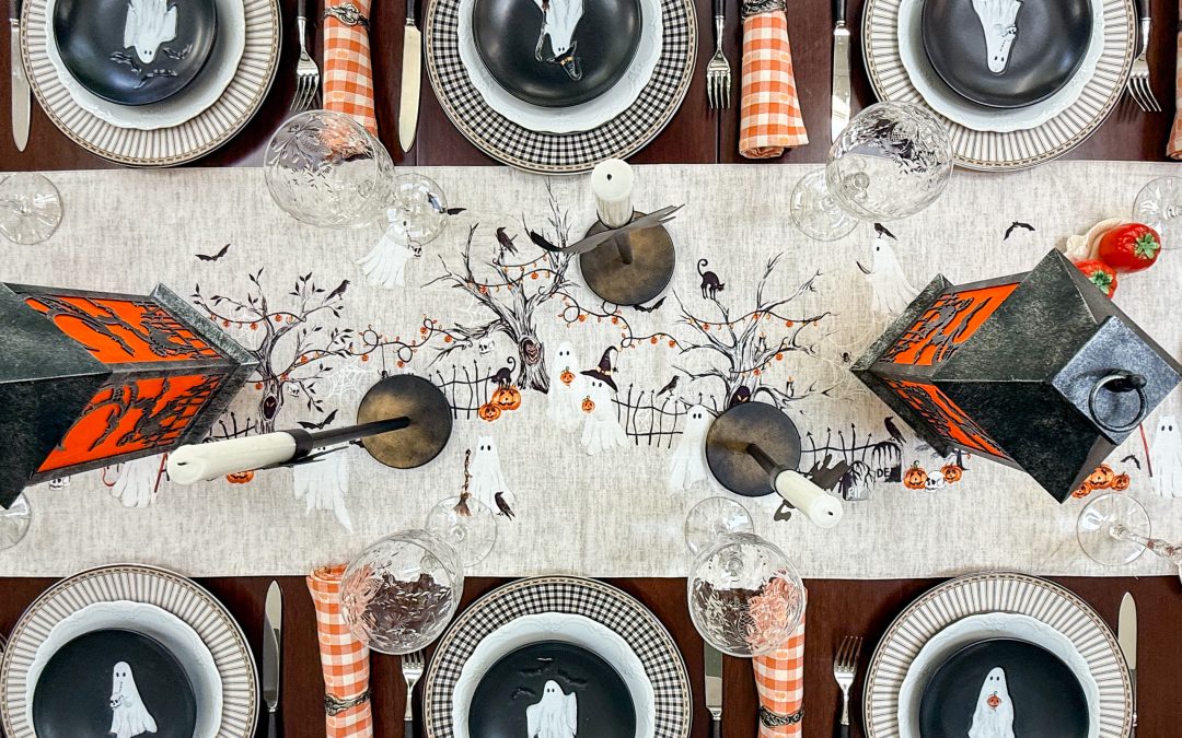 Halloween table with ghost plates, orange gingham napkins and black lanterns along an illustrated runner